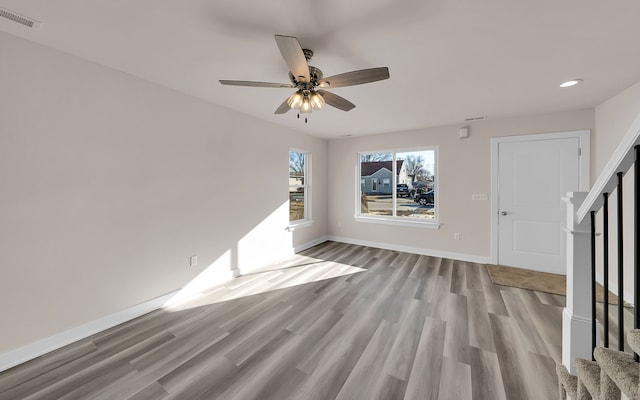 unfurnished living room featuring stairway, wood finished floors, visible vents, baseboards, and ceiling fan