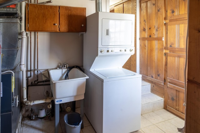 laundry room with stacked washer and dryer, light tile patterned flooring, cabinet space, and a sink