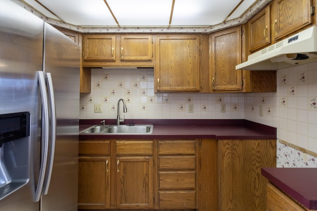 kitchen with stainless steel fridge with ice dispenser, under cabinet range hood, decorative backsplash, brown cabinetry, and a sink