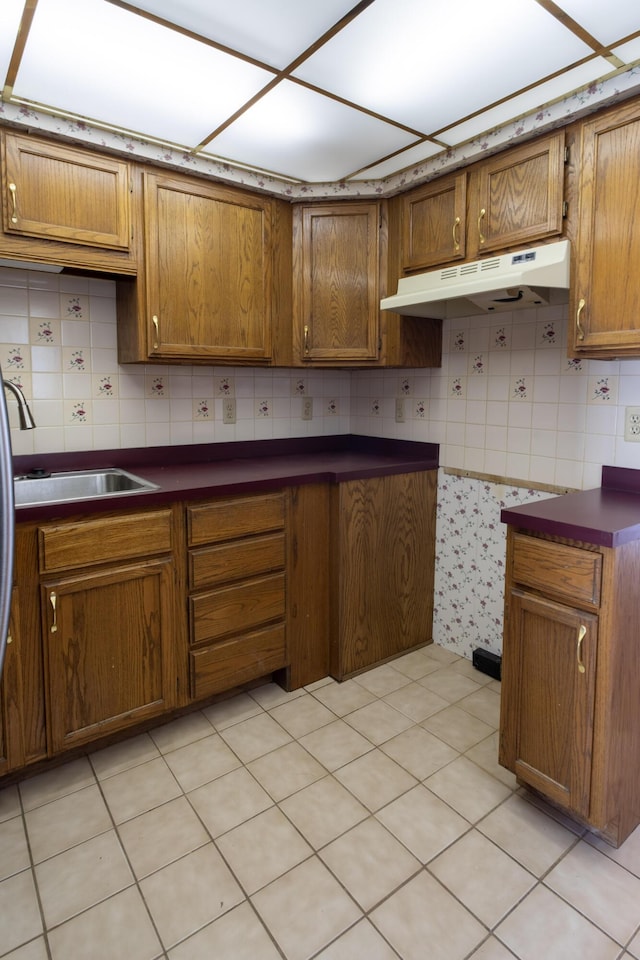 kitchen with under cabinet range hood, a sink, dark countertops, brown cabinetry, and decorative backsplash