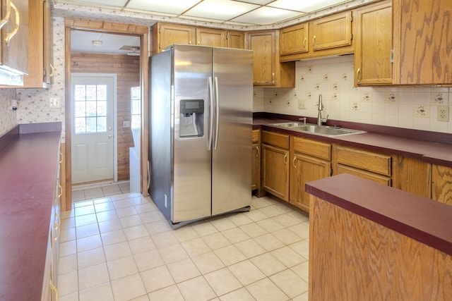 kitchen with wallpapered walls, light tile patterned flooring, stainless steel fridge with ice dispenser, a sink, and brown cabinets