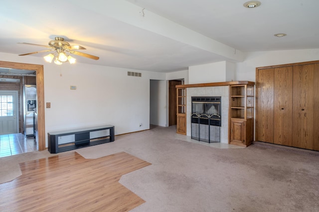 unfurnished living room with light carpet, a ceiling fan, visible vents, and a tile fireplace