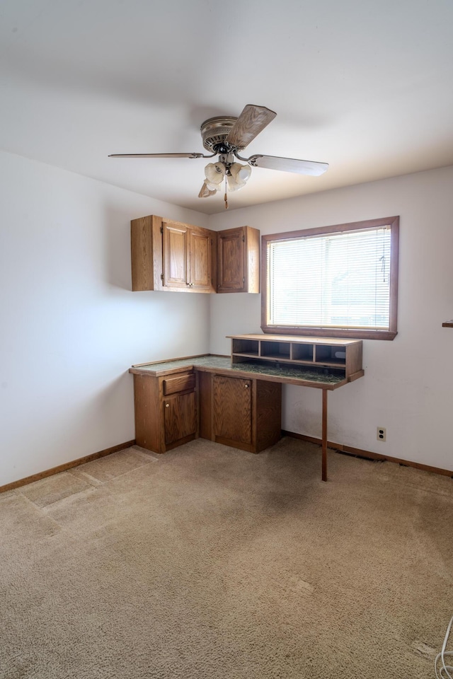 unfurnished office with light carpet, a ceiling fan, and baseboards