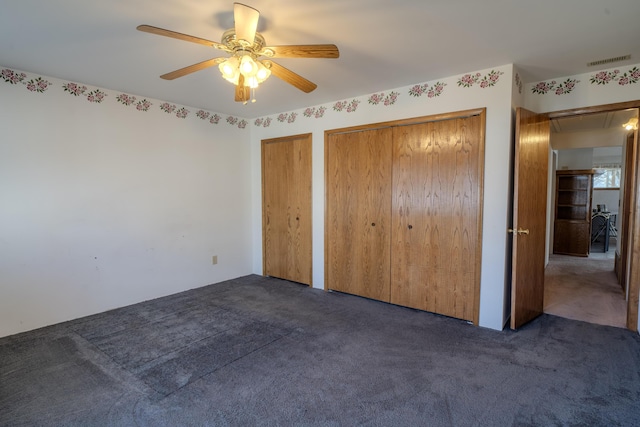 unfurnished bedroom featuring visible vents, two closets, a ceiling fan, carpet floors, and attic access