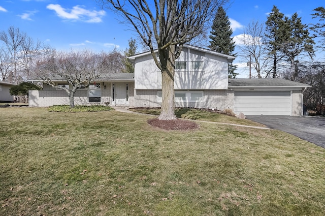 split level home featuring aphalt driveway, brick siding, a garage, and a front lawn