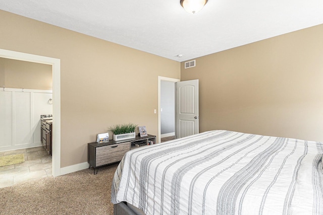 bedroom with visible vents, light colored carpet, ensuite bathroom, and baseboards