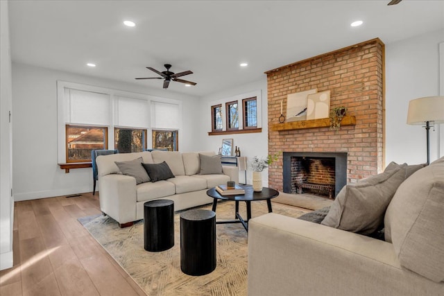 living room with light wood-type flooring, recessed lighting, baseboards, a brick fireplace, and ceiling fan