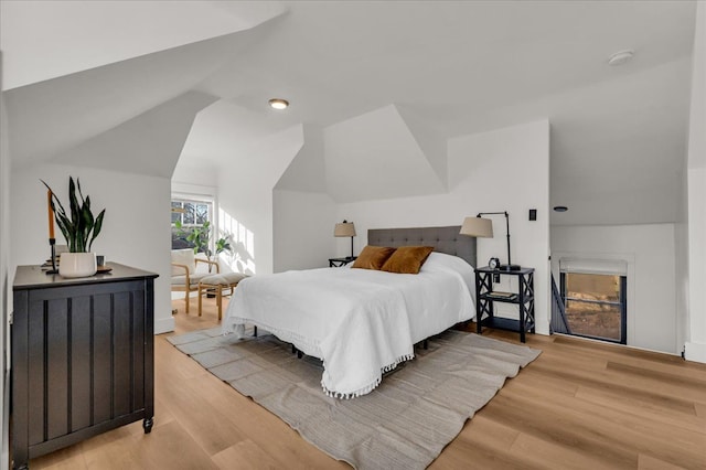 bedroom featuring light wood-style floors, a fireplace, and vaulted ceiling