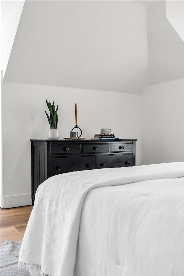 bedroom featuring baseboards, light wood-type flooring, and lofted ceiling