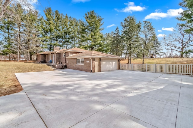 view of home's exterior with driveway, fence, a garage, brick siding, and a chimney