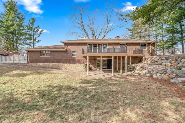 rear view of house featuring brick siding, a wooden deck, a chimney, and a yard