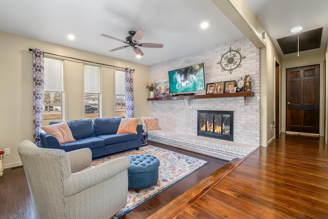 living area with baseboards, attic access, a fireplace, wood finished floors, and a ceiling fan