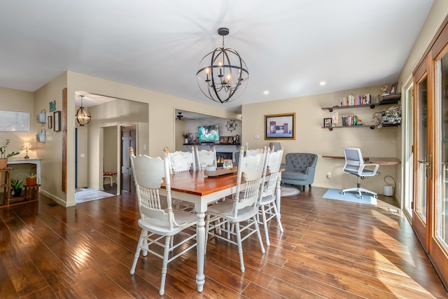 dining room featuring a warm lit fireplace, baseboards, an inviting chandelier, and wood finished floors