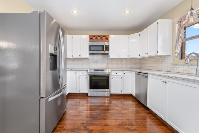 kitchen with light stone counters, a sink, decorative backsplash, stainless steel appliances, and white cabinetry