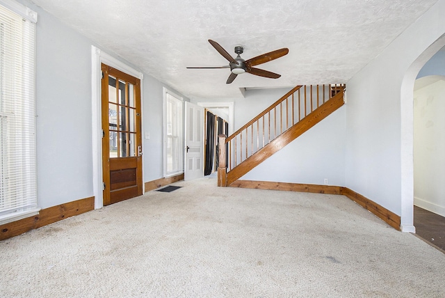 carpeted entryway with ceiling fan, baseboards, stairs, arched walkways, and a textured ceiling