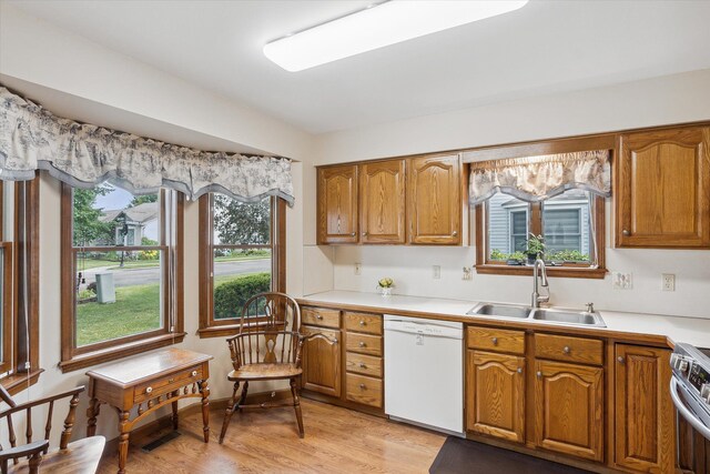 kitchen featuring brown cabinetry, light wood-style flooring, stainless steel electric range, white dishwasher, and a sink