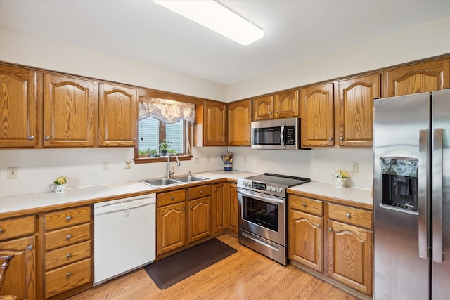 kitchen featuring light wood-style flooring, a sink, appliances with stainless steel finishes, brown cabinetry, and light countertops