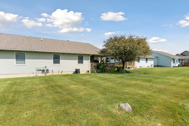 rear view of house with a yard, central AC, and roof with shingles