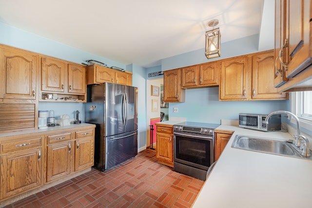 kitchen with a sink, appliances with stainless steel finishes, brown cabinetry, light countertops, and brick floor