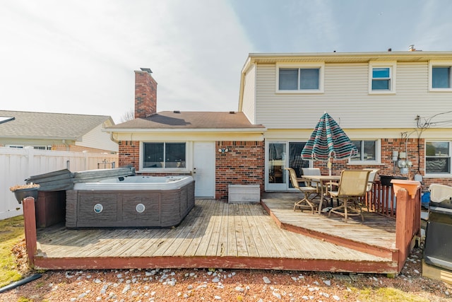 rear view of house with brick siding, a wooden deck, and a hot tub