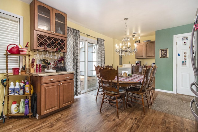 dining space featuring a bar, a notable chandelier, dark wood-style floors, and baseboards