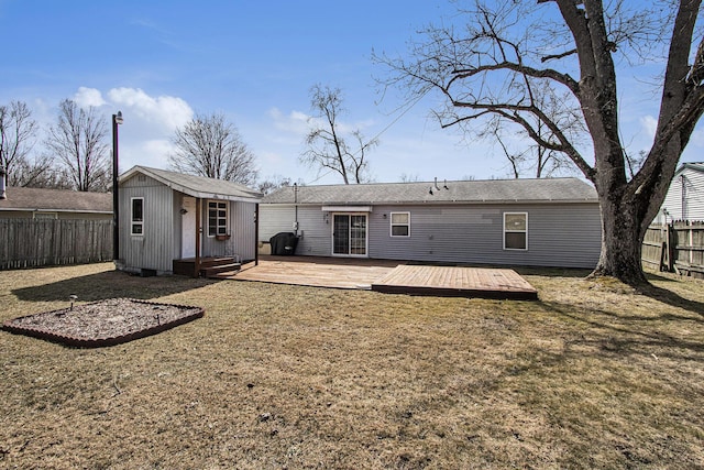 rear view of property featuring an outbuilding, a deck, a lawn, and a fenced backyard