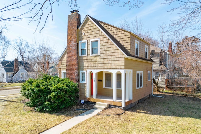 view of front facade with a front yard, a porch, a chimney, and fence