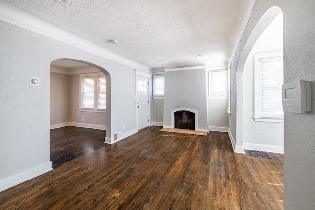 unfurnished living room featuring arched walkways, visible vents, wood-type flooring, and a textured ceiling