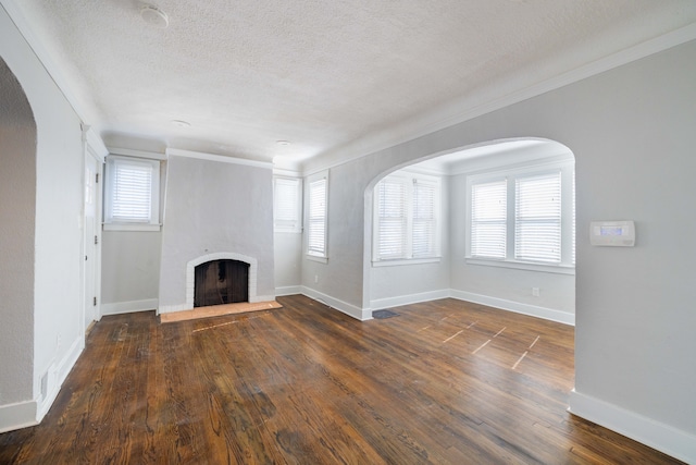 unfurnished living room with a textured ceiling, wood finished floors, arched walkways, a fireplace, and baseboards