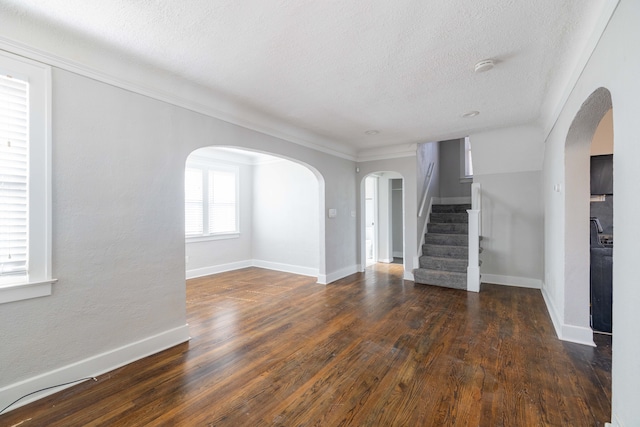 unfurnished living room with baseboards, arched walkways, a textured ceiling, and wood finished floors