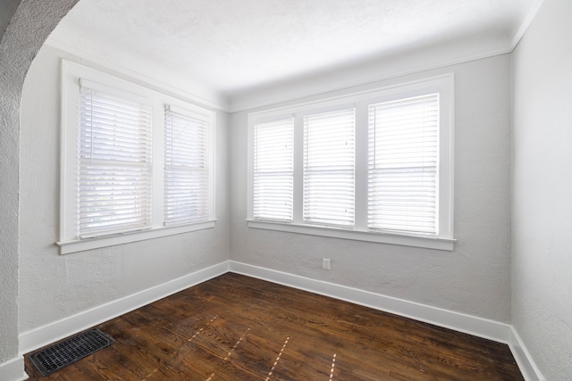 unfurnished room with dark wood-type flooring, baseboards, visible vents, and a textured wall