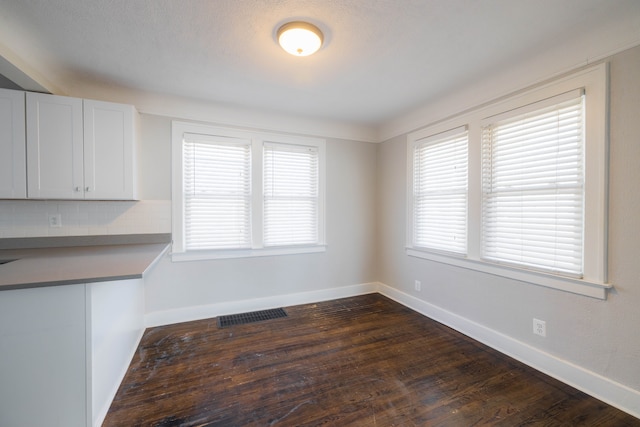 unfurnished dining area with visible vents, baseboards, and dark wood-style flooring