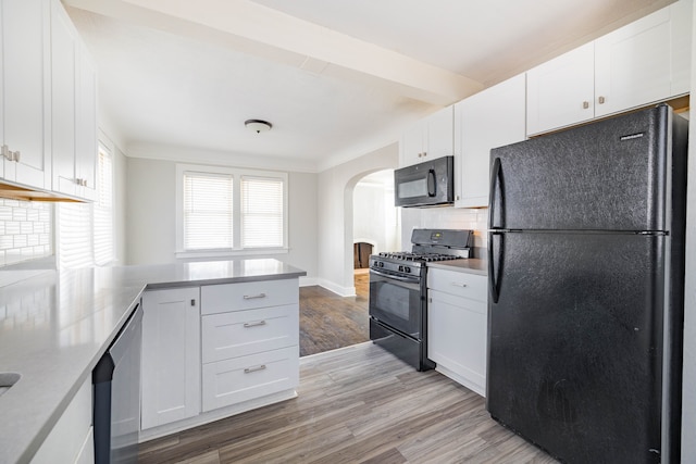 kitchen with tasteful backsplash, light wood-style flooring, a peninsula, arched walkways, and black appliances