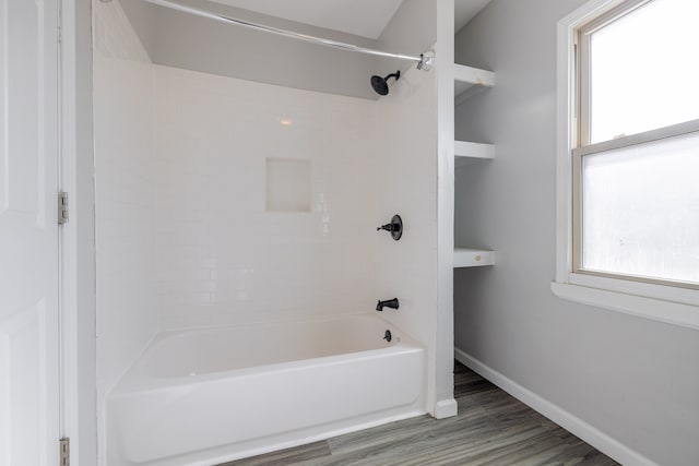 bathroom featuring wood finished floors, washtub / shower combination, and baseboards