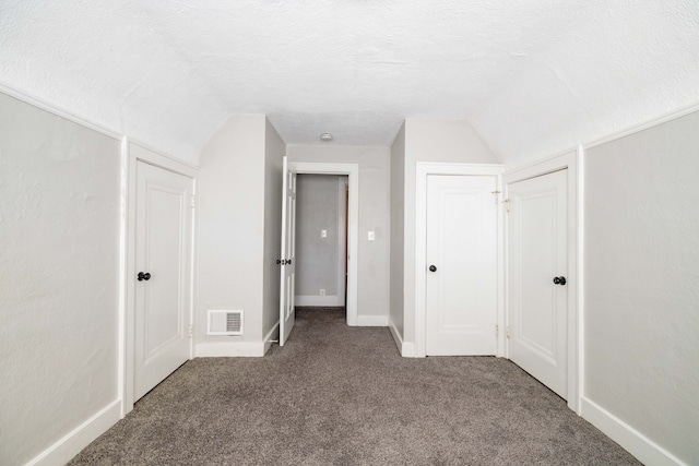 unfurnished bedroom with visible vents, a textured ceiling, carpet floors, baseboards, and vaulted ceiling