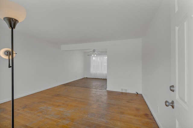 unfurnished room with ceiling fan, wood finished floors, visible vents, and baseboards