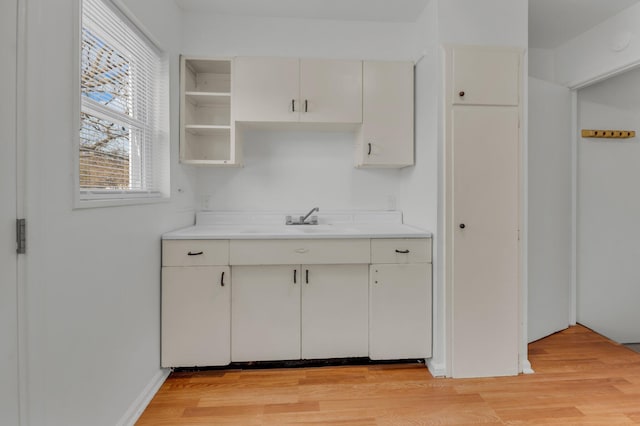 kitchen with white cabinetry, light countertops, light wood-style floors, and a sink