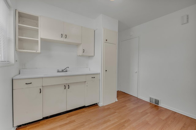 kitchen featuring light countertops, visible vents, light wood finished floors, and a sink