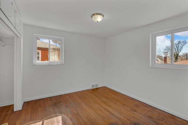 unfurnished bedroom with hardwood / wood-style floors, visible vents, baseboards, and a closet