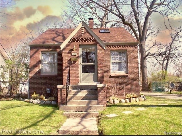 view of front of house featuring brick siding, a chimney, a front yard, and fence