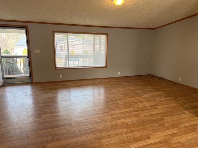 empty room with crown molding, light wood finished floors, and a textured ceiling