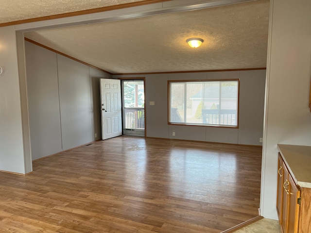 unfurnished living room with lofted ceiling, light wood-style floors, crown molding, and a textured ceiling