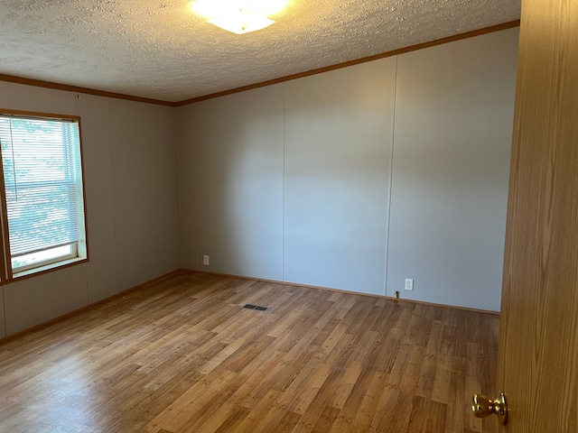 unfurnished room with visible vents, a textured ceiling, crown molding, and wood finished floors