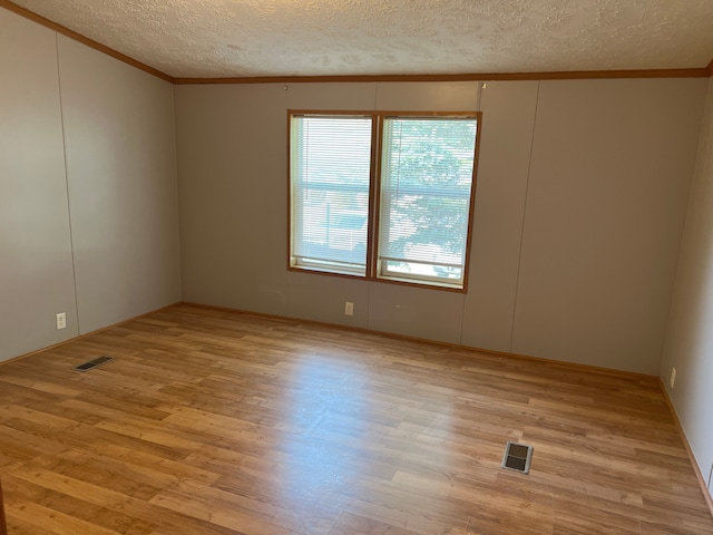 unfurnished room with a textured ceiling, crown molding, visible vents, and light wood-type flooring