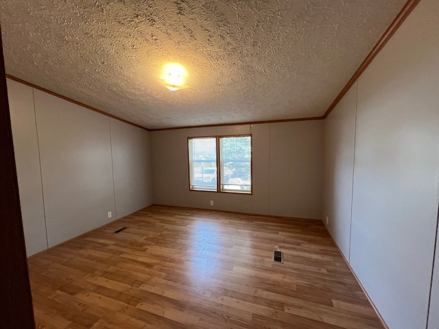 empty room featuring a textured ceiling, light wood-style flooring, visible vents, and ornamental molding