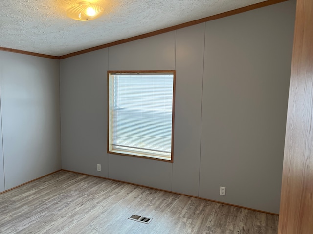 unfurnished room with visible vents, lofted ceiling, ornamental molding, wood finished floors, and a textured ceiling