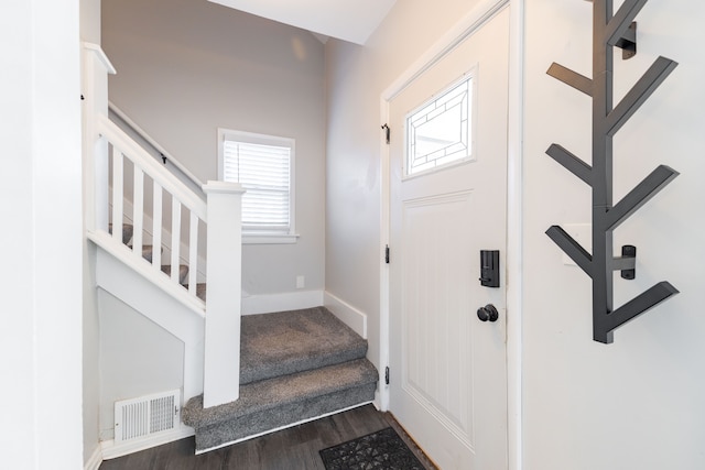 foyer entrance featuring dark wood-type flooring, stairway, baseboards, and visible vents