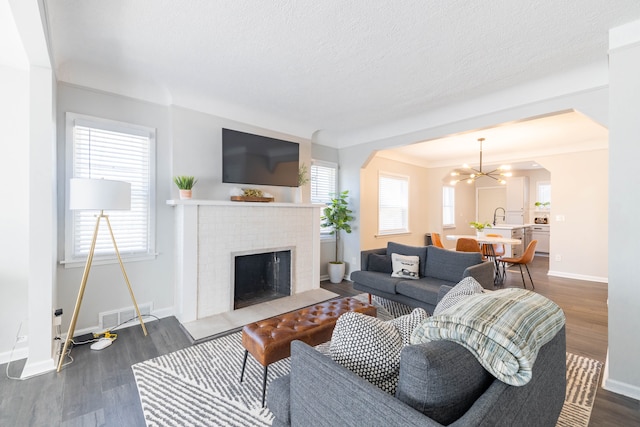 living room with visible vents, a fireplace with flush hearth, a notable chandelier, dark wood finished floors, and arched walkways