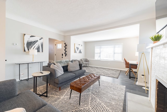 living room with a fireplace with flush hearth, a textured ceiling, baseboards, and wood finished floors