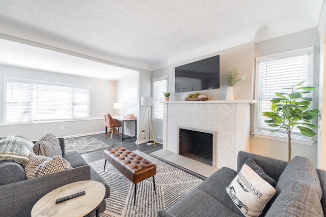 living area featuring a brick fireplace, a textured ceiling, baseboards, and wood finished floors